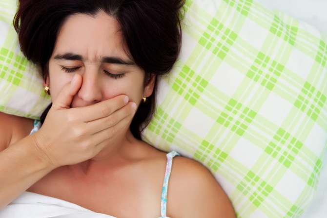 Hispanic woman laying in bed and covering her mouth to avoid coughing or womiting
