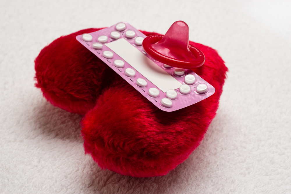 Oral contraceptive pills condom on red heart