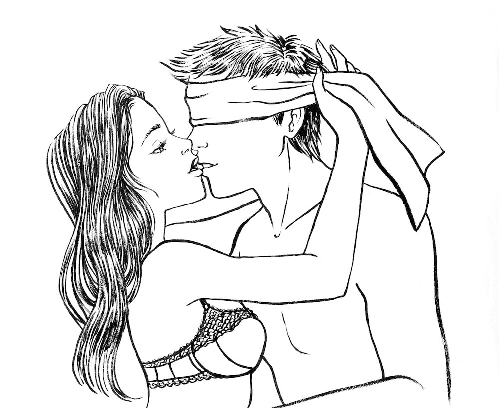 woman tying blindfold on man while kissing him
